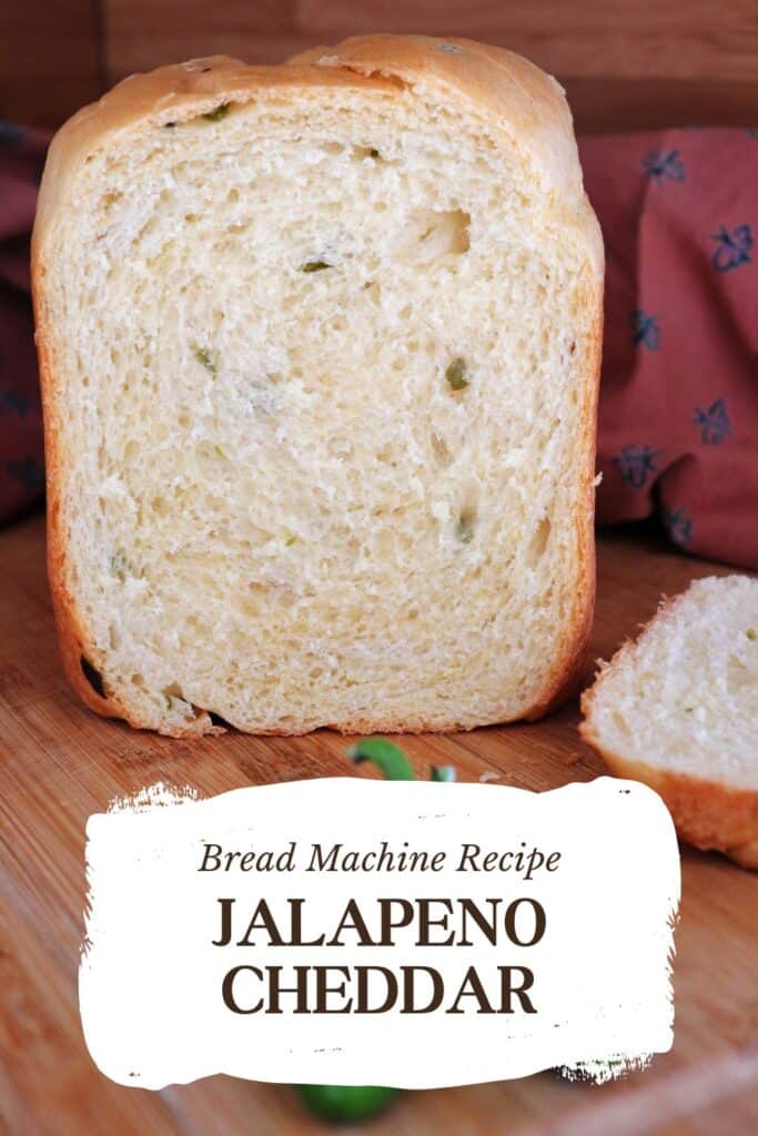 A loaf of bread with end cut off exposing pieces of green jalapeno peppers inside sits on a board. Text overlay reads: Bread Machine Recipe Jalapeno Cheddar.