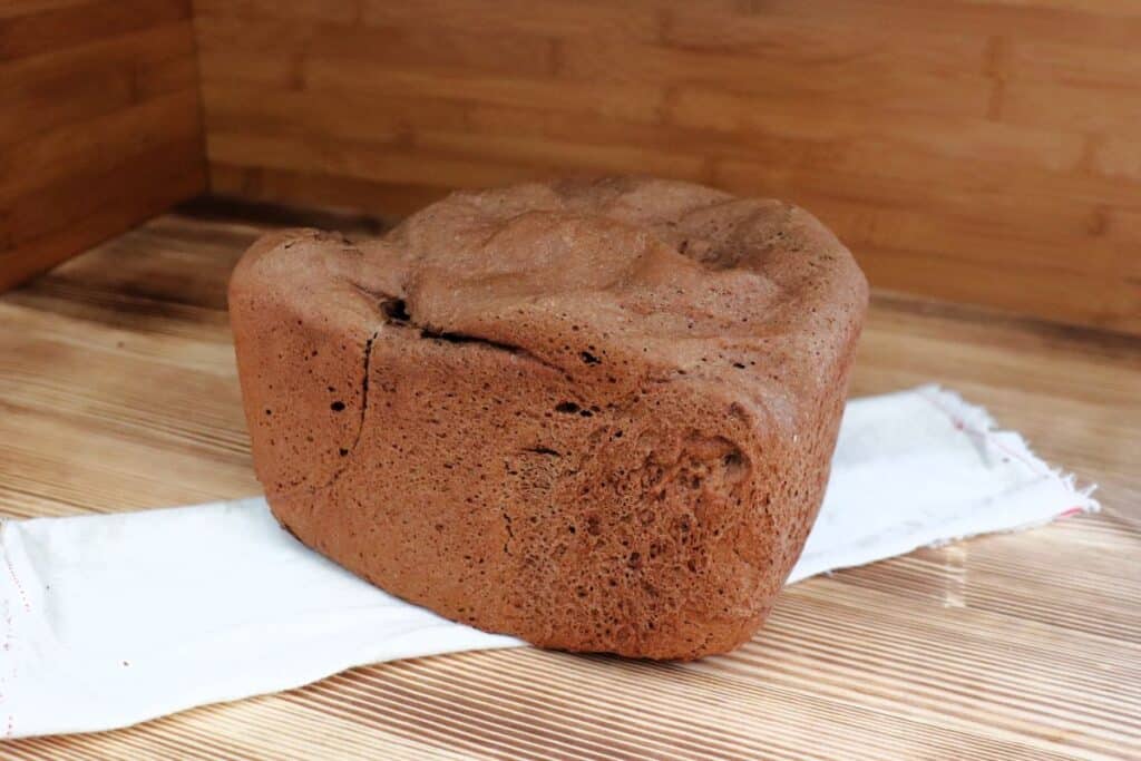A loaf of dark bread sits on a white cloth on a table. 