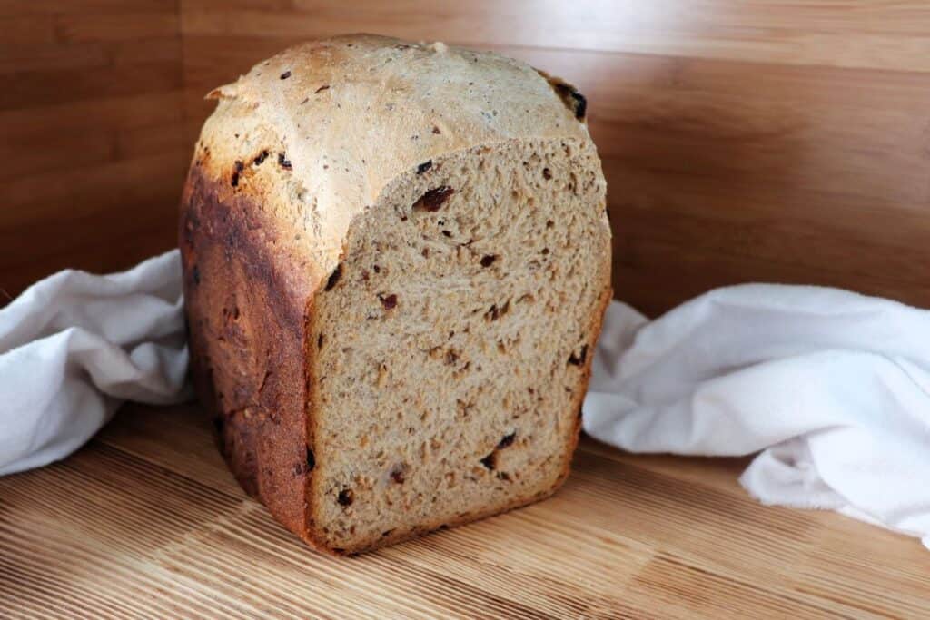 A loaf of cinnamon raisin bread sits on a board with the end cut off, exposing the inside.