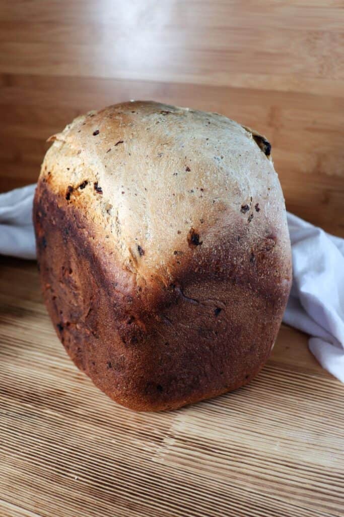 A loaf of cinnamon raisin bread sits on a table with a cloth behind it.