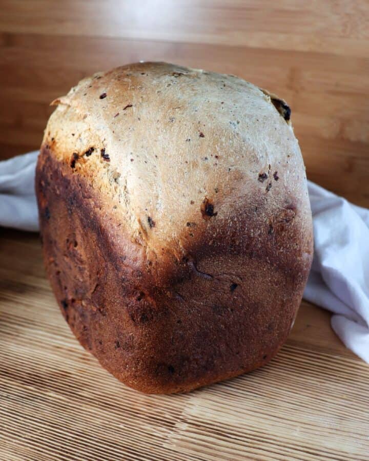 A loaf of cinnamon raisin bread sits on a board with a cloth behind it.