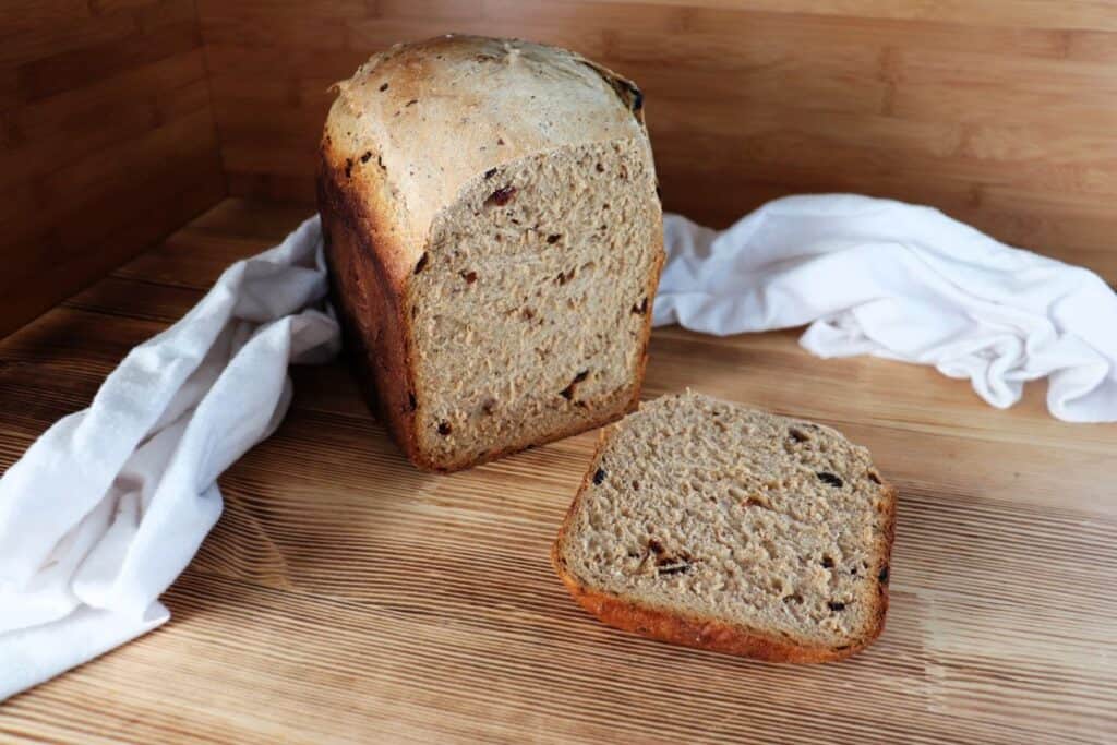 A loaf of cinnamon raisin bread sits on a board with the end cut off, exposing the inside. The cut off slice sits to the side. 