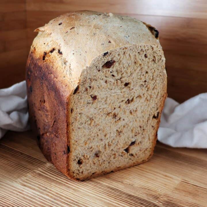 A loaf of cinnamon raisin bread sits on a board with the end cut off, exposing the inside.