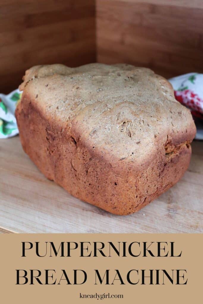 A loaf of pumpernickel bread sits on a board, a floral cloth in the background. Text overlay reads: Pumpernickel Bread Machine."