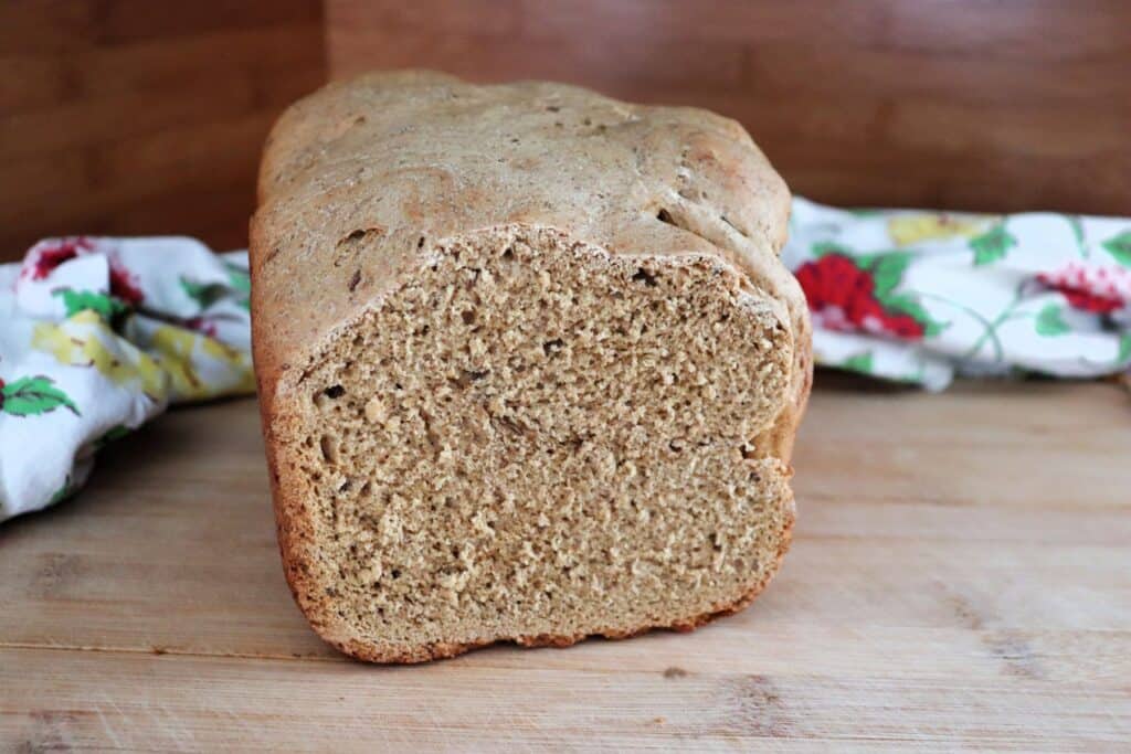A loaf of pumpernickel bread sits on a table with a floral cloth behind it. The end has been cut off, exposing the bread inside.