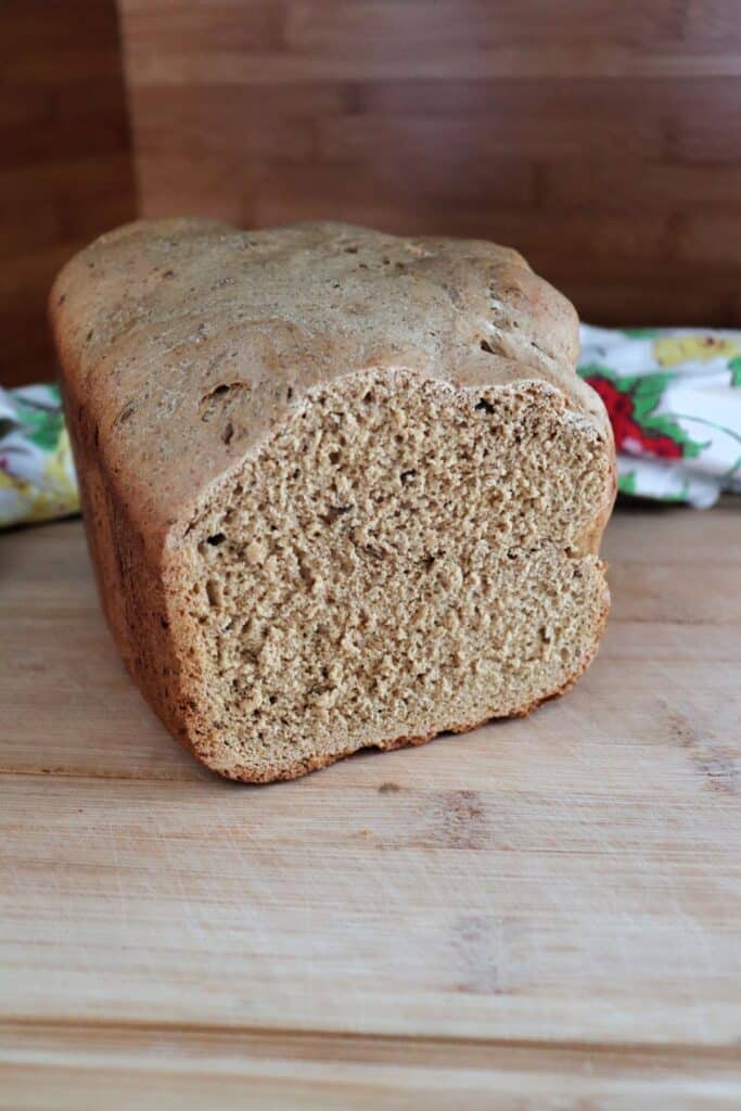 A loaf of pumpernickel bread sits on a table with a floral cloth behind it. The end has been cut off, exposing the bread inside.