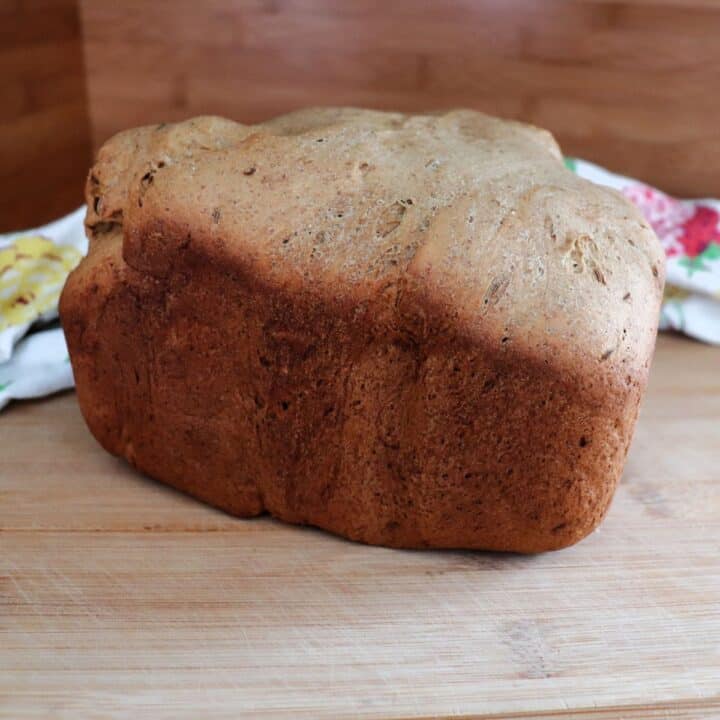 A loaf of pumpernickel bread sits on a wooden board as seen from the side.