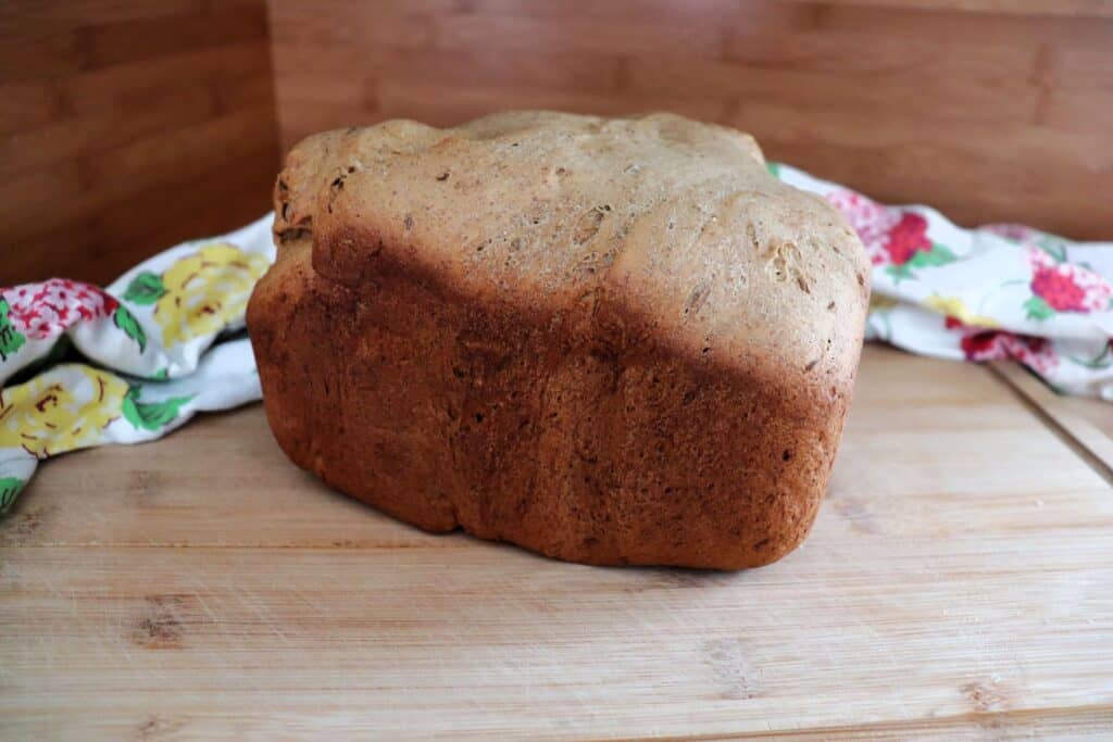 A loaf of pumpernickel as seen from its side sits on a board with a floral cloth behind it.