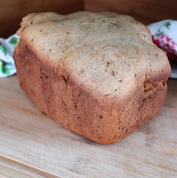 A loaf of pumpernickel bread sits on a a board with a floral cloth behind it.