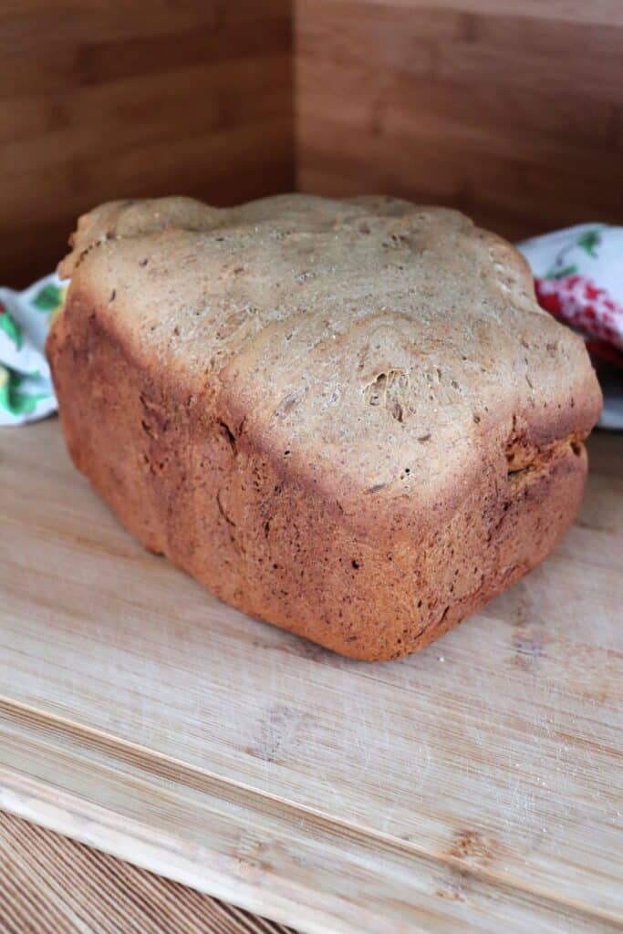 A loaf of pumpernickel bread sits on a a board with a floral cloth behind it.