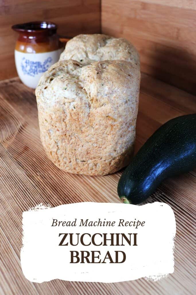 A loaf of bread sits on a board with a fresh zucchini next to it. In the background is a clay pitcher. Text overlay reads: Bread Machine Recipe - Zucchini Bread.