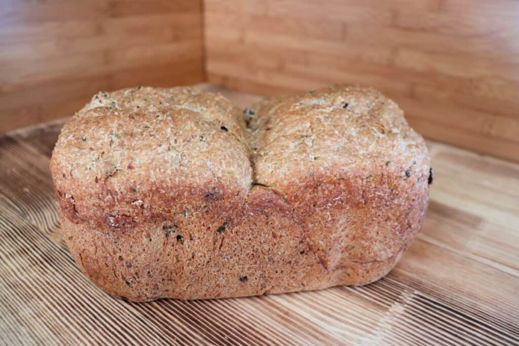 A loaf of zucchini raisin bread as seen from the side sits on a board. 
