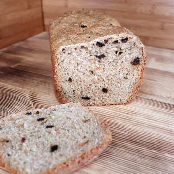 A loaf of zucchini raisin bread with the end cut off sits on a board. The heel of the bread sits in front of the loaf.
