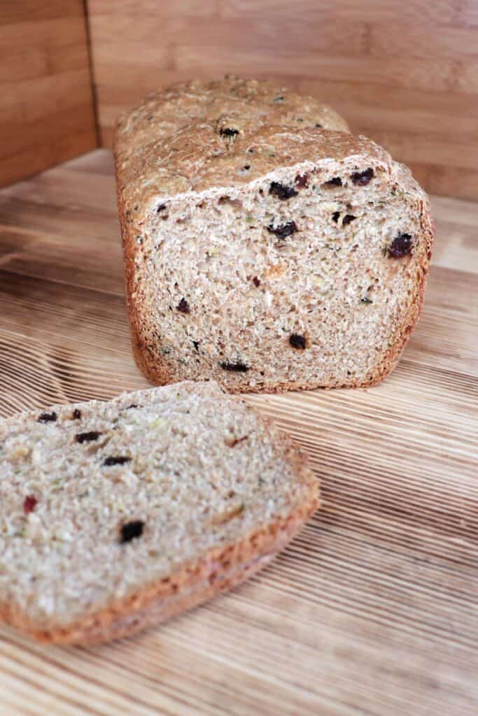A loaf of zucchini raisin bread with the end cut off sits on a board. The heel of the bread sits in front of the loaf. 