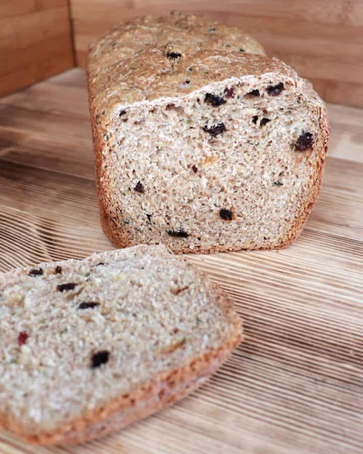 A loaf of zucchini raisin bread with the end cut off sits on a board. The heel of the bread sits in front of the loaf.