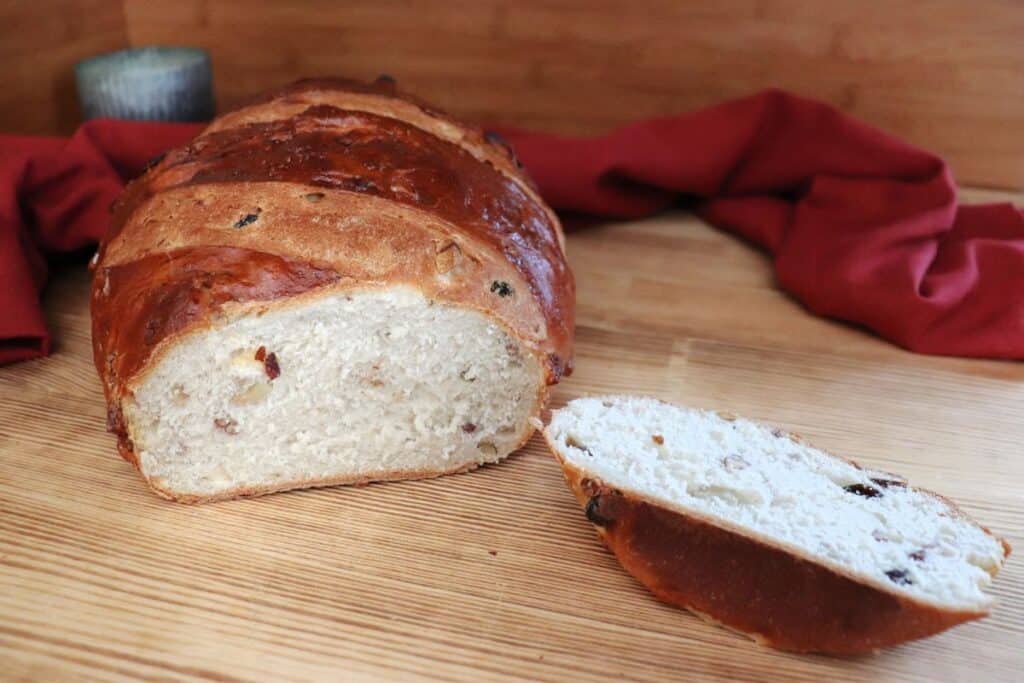 A loaf of apple raisin bread with the end cut of exposing the insides sits on a board, the heel sits next to the loaf. A red cloth and candle can be seen in the background. 