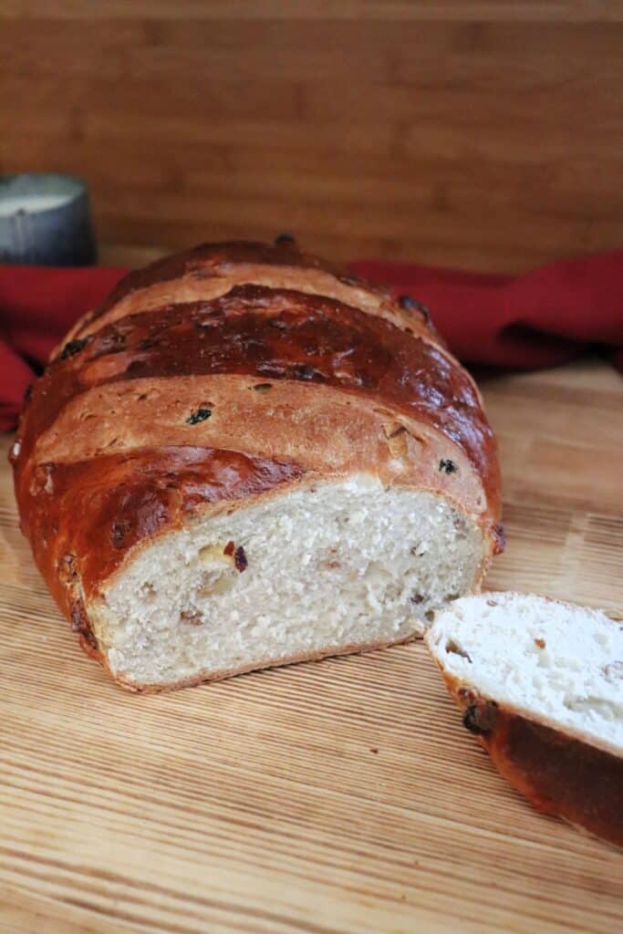 A loaf of apple raisin walnut bread with the end cut of exposing the insides sits on a board. 