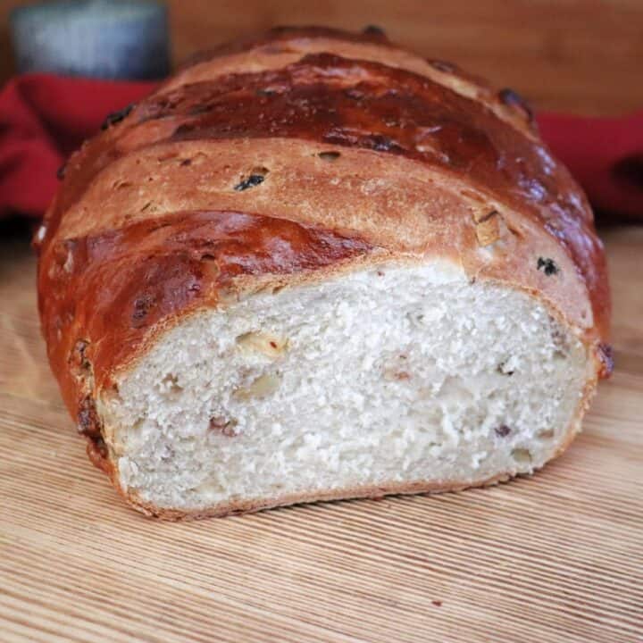 A loaf of apple raisin bread with the end cut off exposing the insides sits on a board.